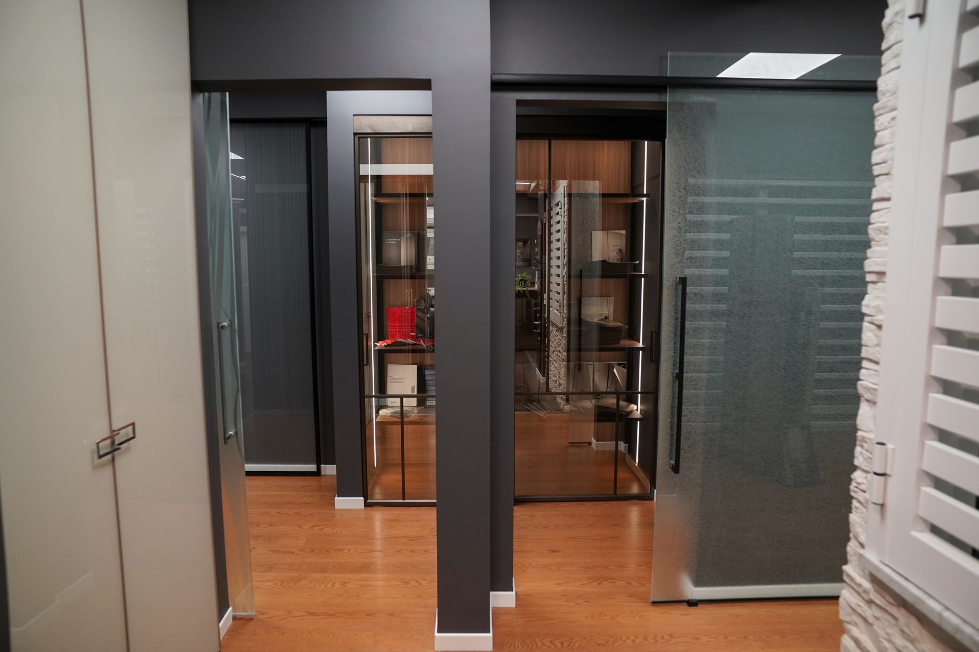 Corridoio con porte scorrevoli in vetro, vetrine e colonne grigio scuro.
