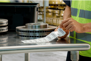 Person peels a label, ready to apply it to a metal brake rotor in a warehouse setting.