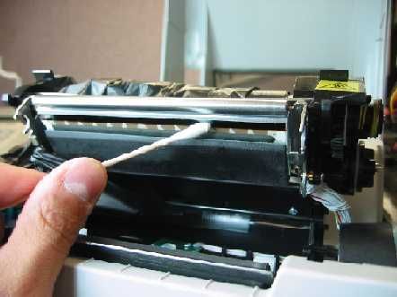 A hand uses a cotton swab to clean a printer's internal metal print head mechanism.