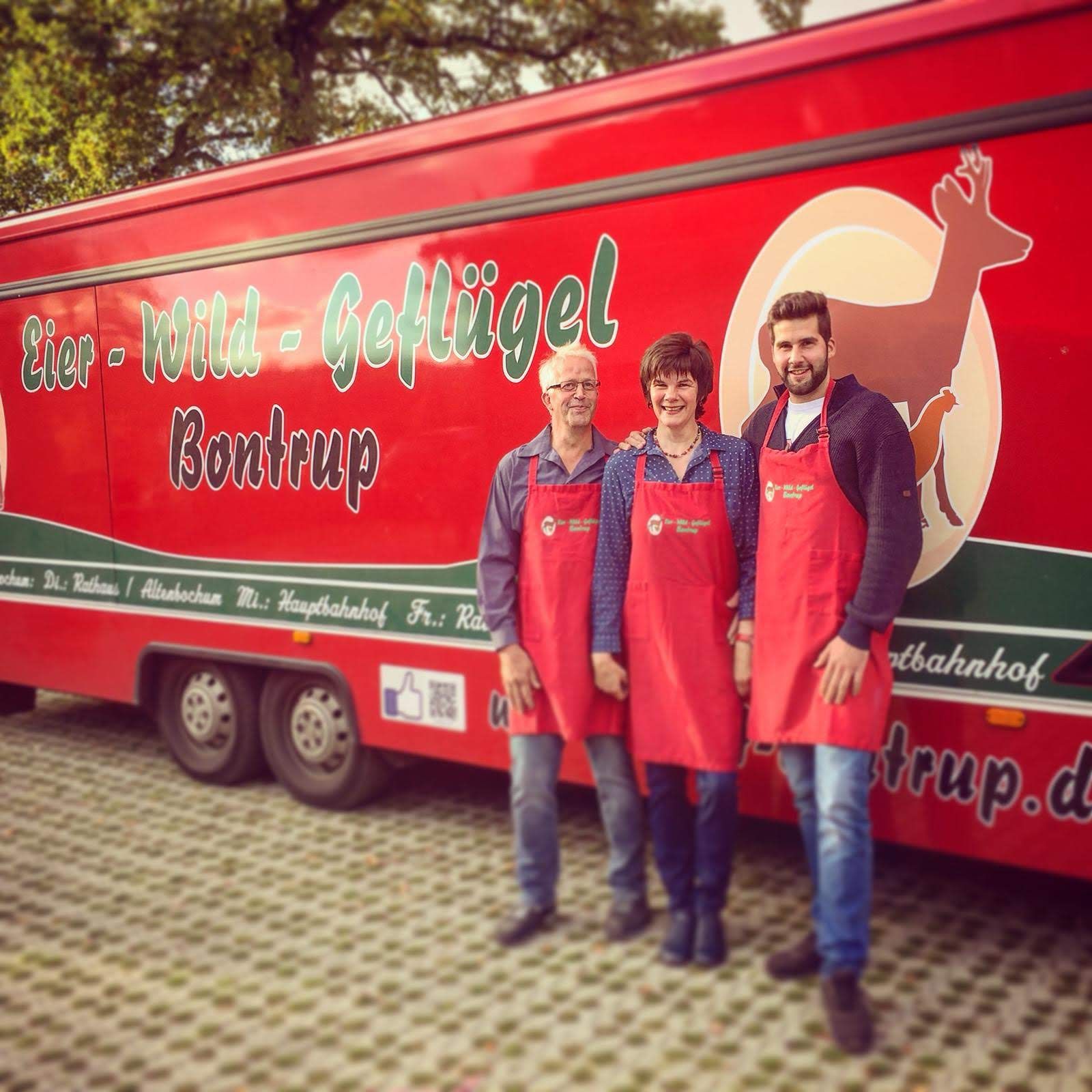 Drei Personen stehen vor einem roten Anhänger mit der Aufschrift „wild-geflügel“