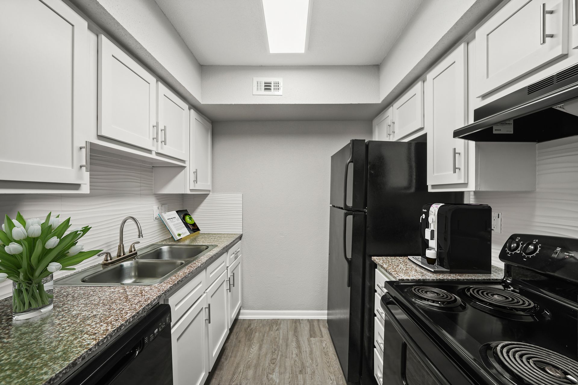 A kitchen with white cabinets , a black refrigerator , a stove , and a sink.