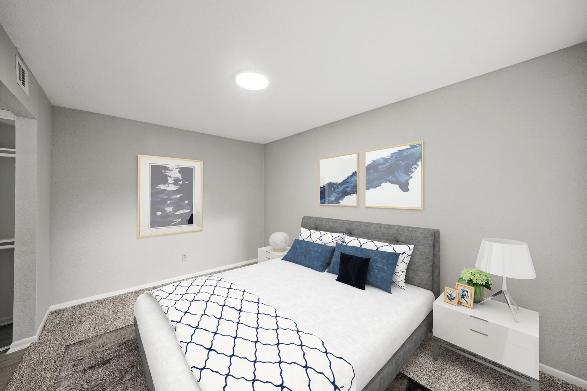 A bedroom with a bed , nightstand , lamp and paintings on the wall.