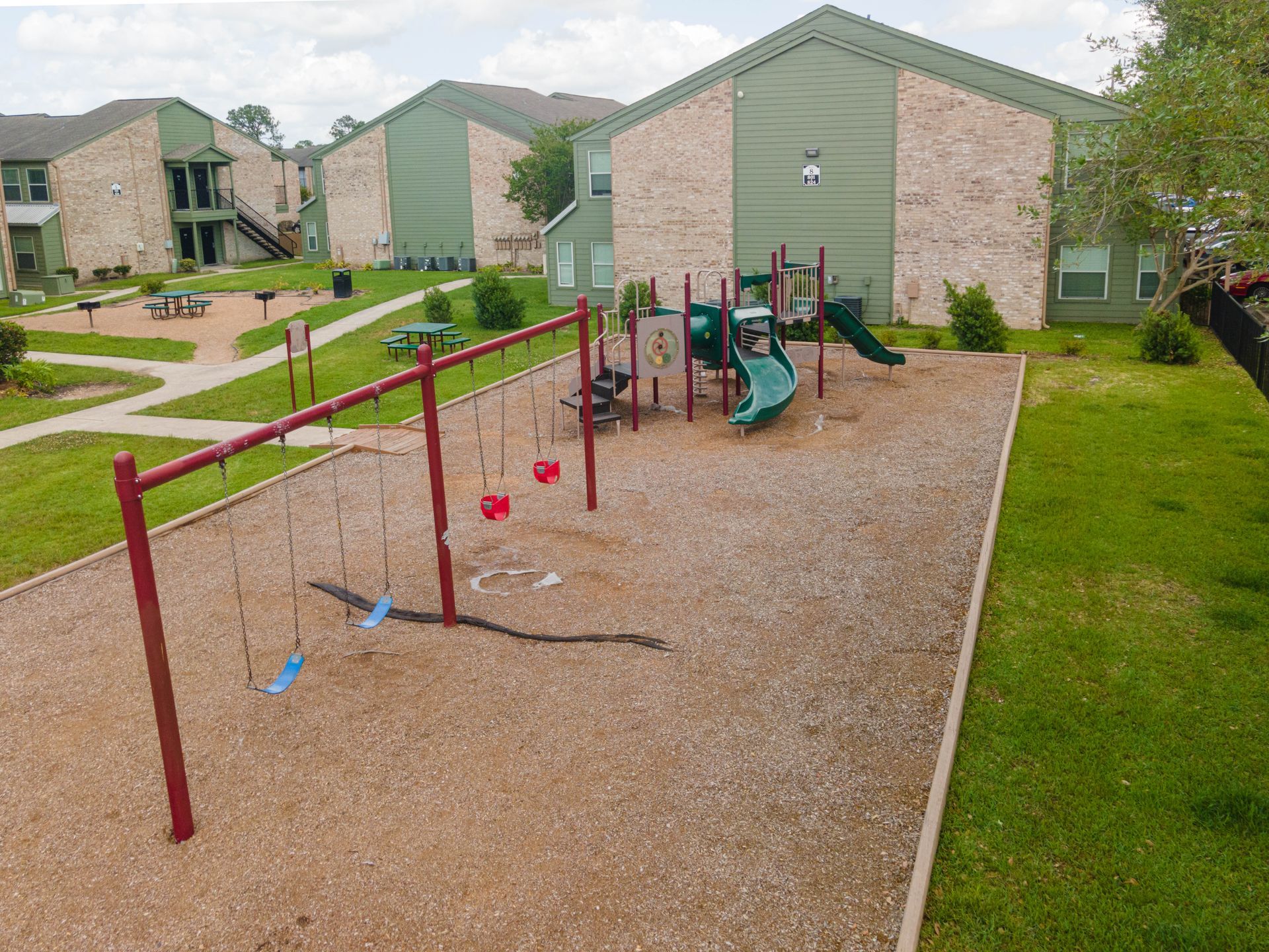 A playground with swings and a slide in front of a brick building.