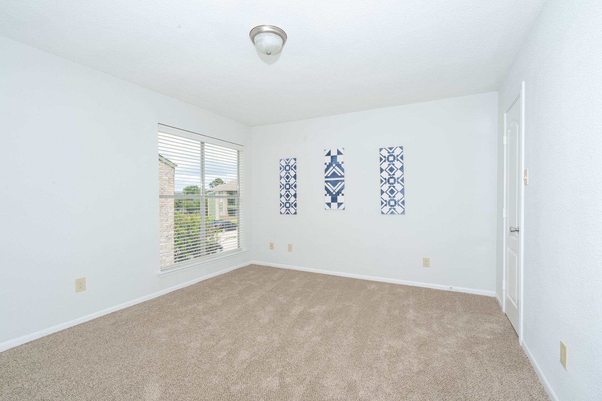 An empty bedroom with a carpeted floor and two windows.