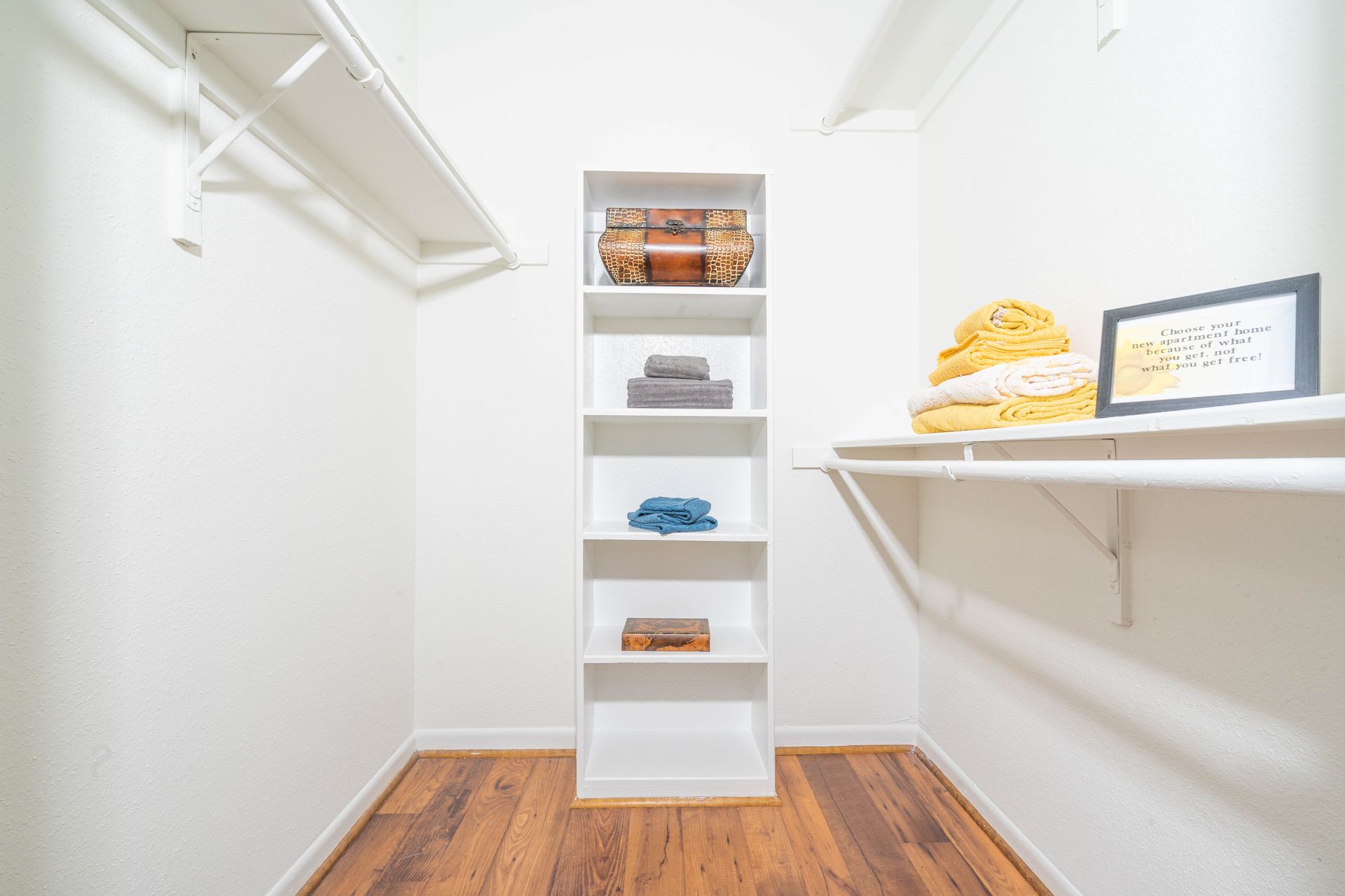 A walk in closet with hardwood floors and white shelves.