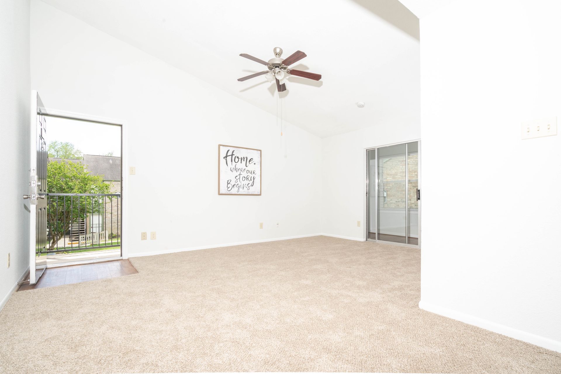 An empty living room with a ceiling fan and sliding glass doors.