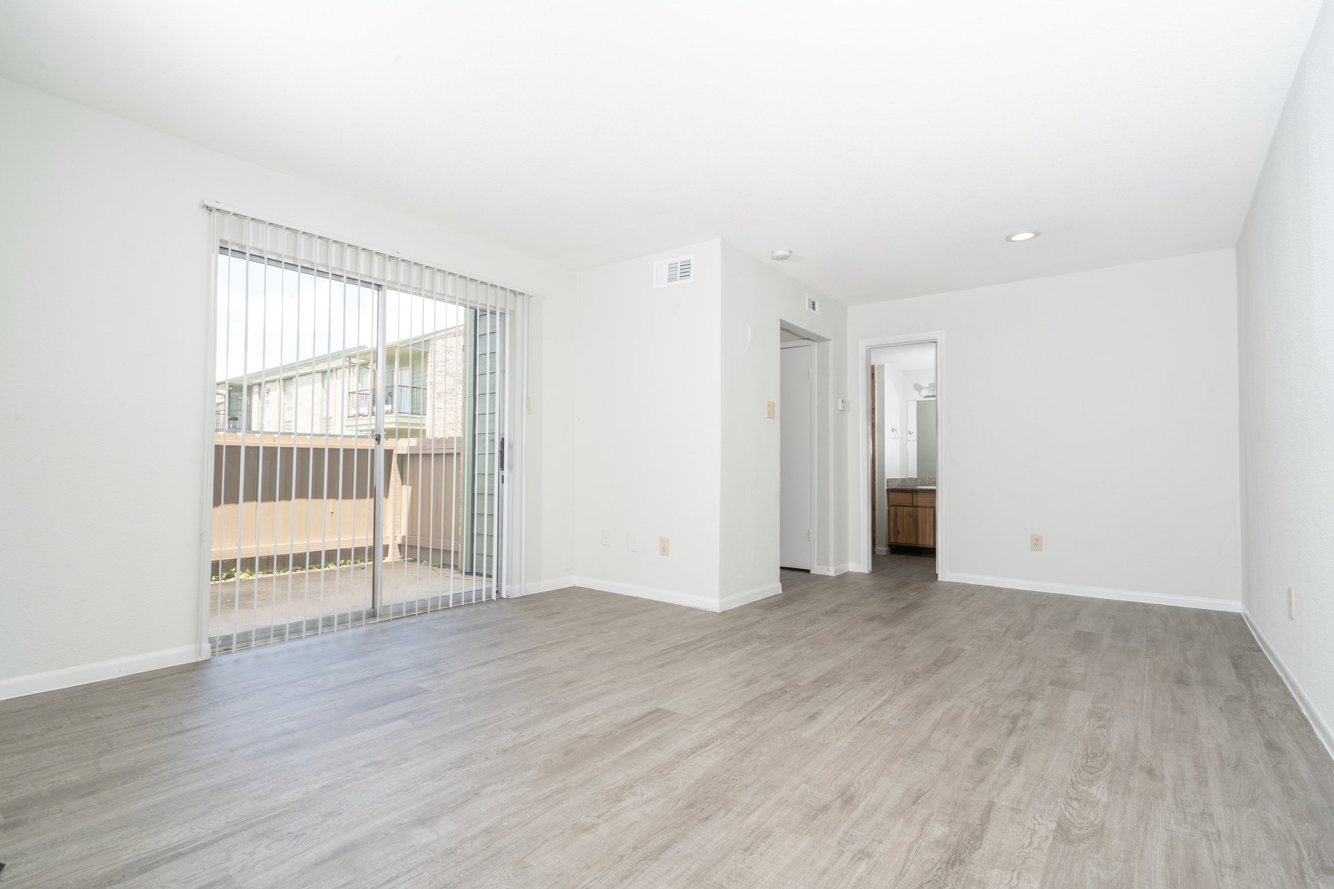 An empty living room with hardwood floors and sliding glass doors leading to a balcony.