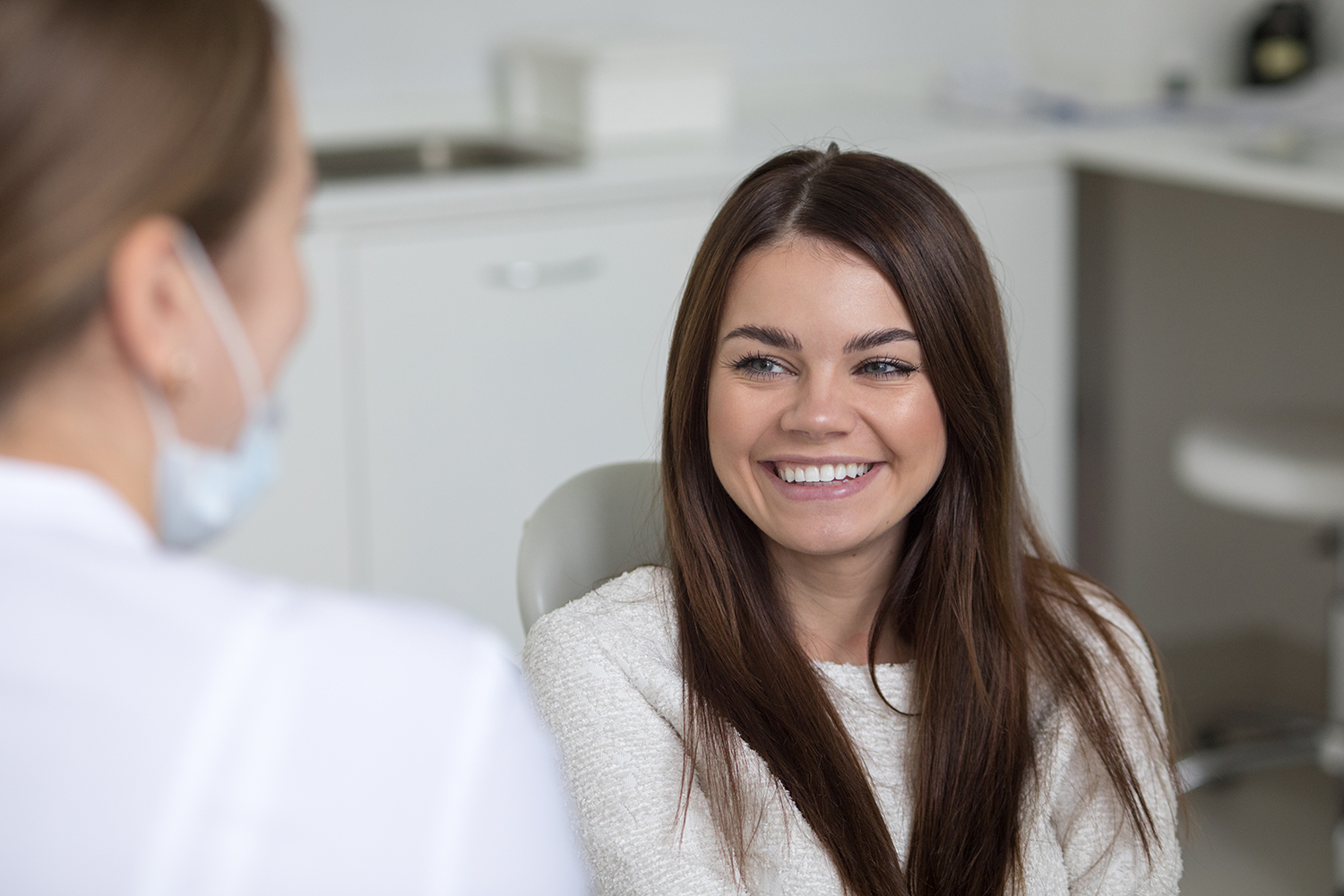 girl sitting in dental chair smiling while talking to a dental assistant
