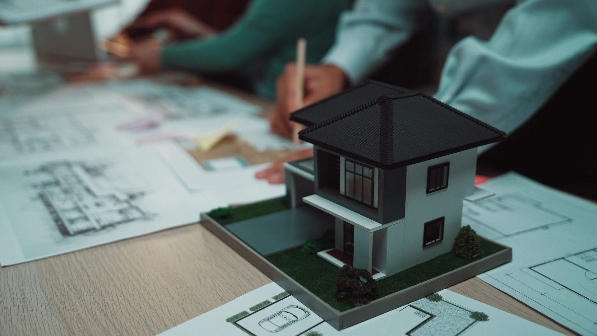 A scale model of a house sits on a desk covered in architectural blueprints.