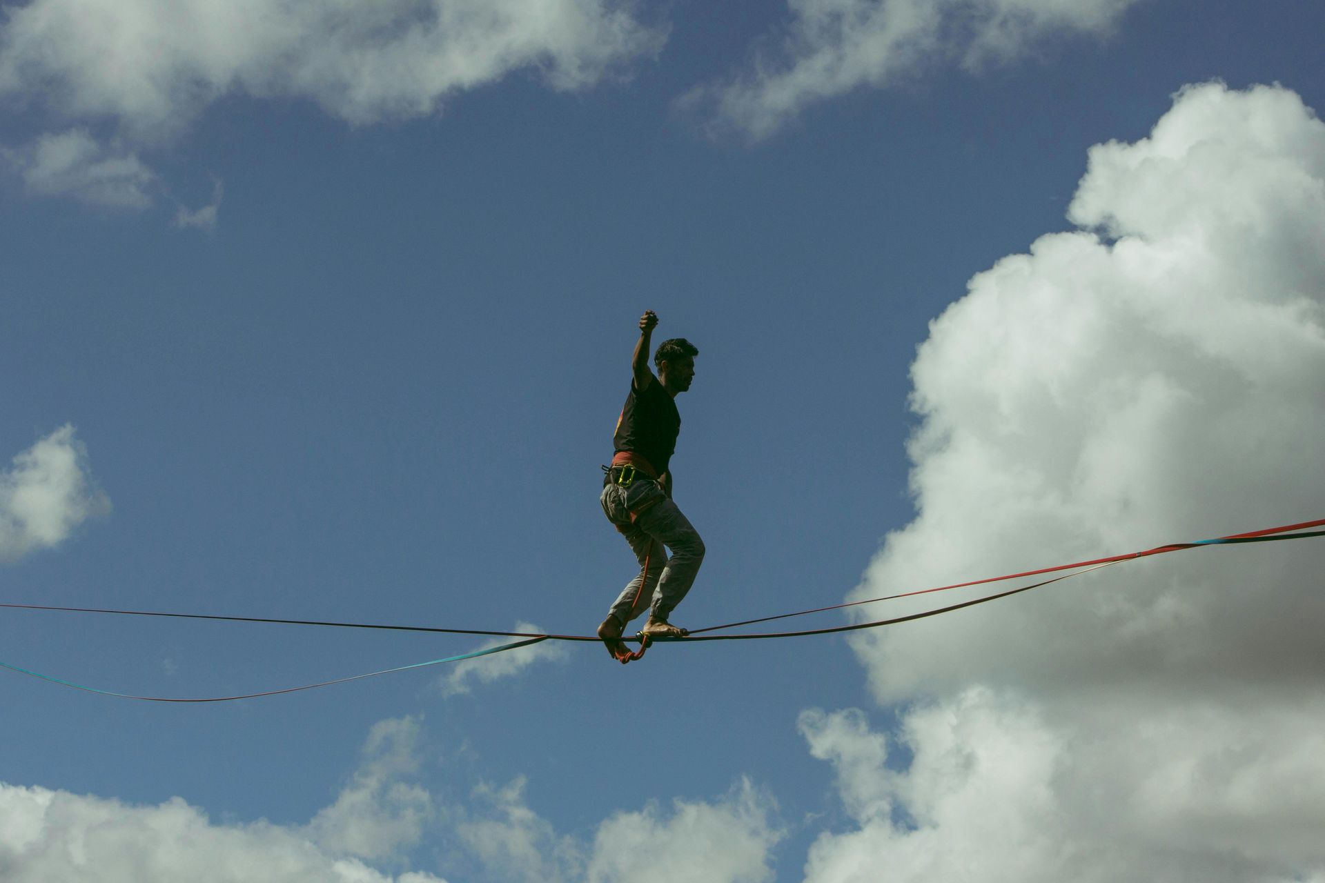 Man on a tightrope against the backdrop of a blue sky with white fluffy clouds