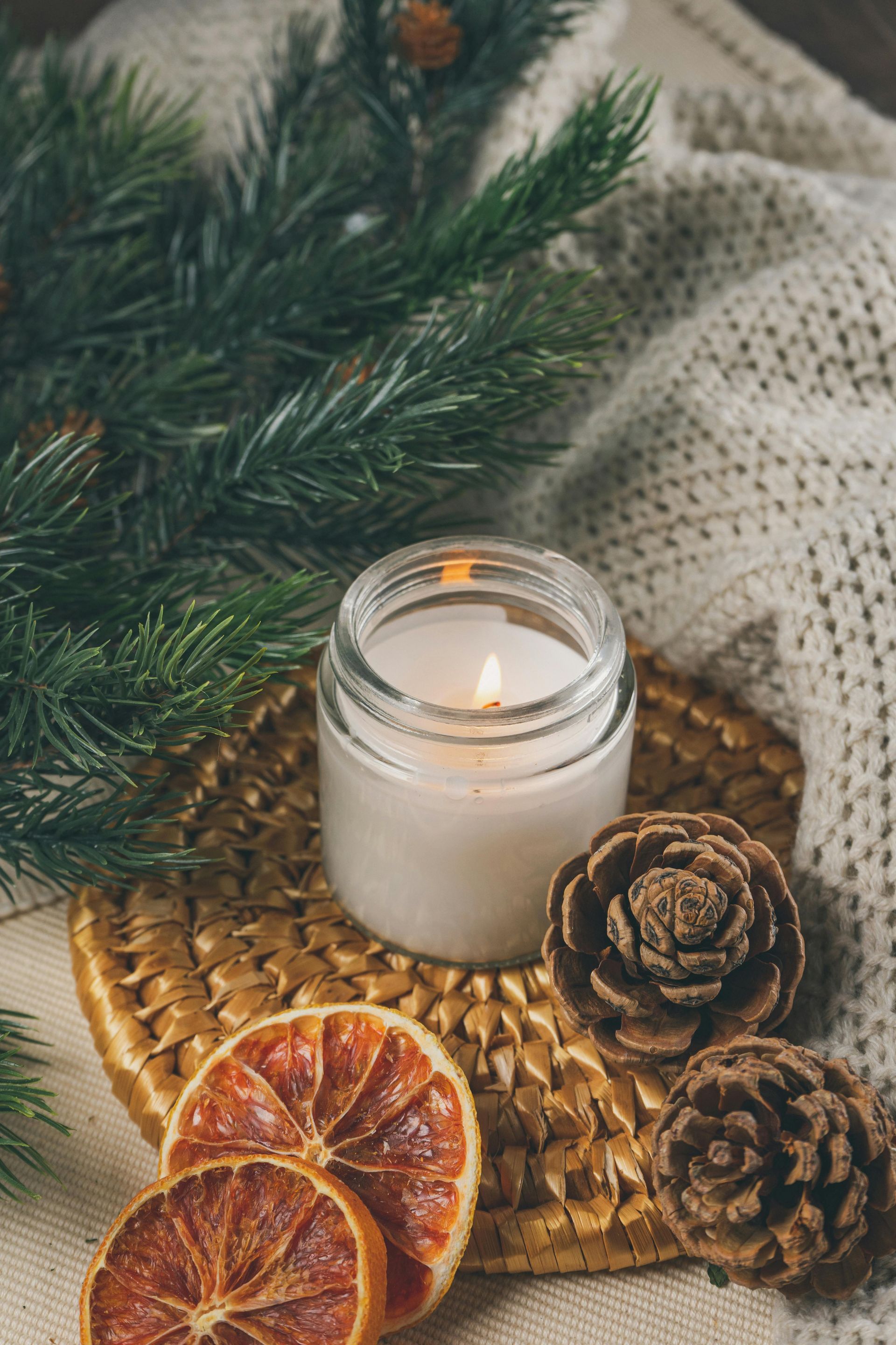 White candle in a jar surrounded by pine branches, pine cones and dried orange slices