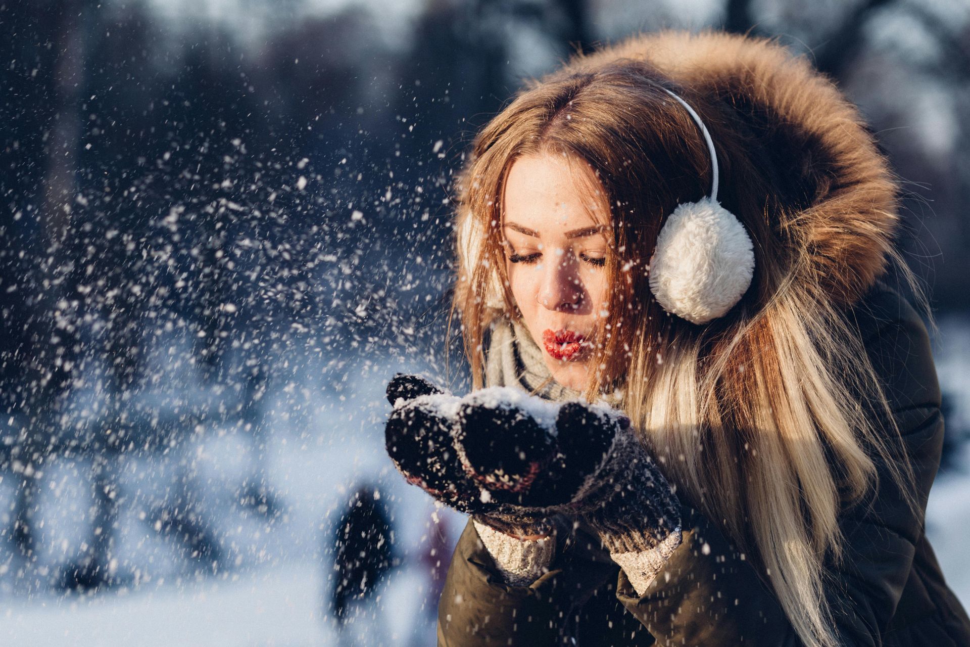 Woman wearing winter clothes blowing a handful of snow into the air