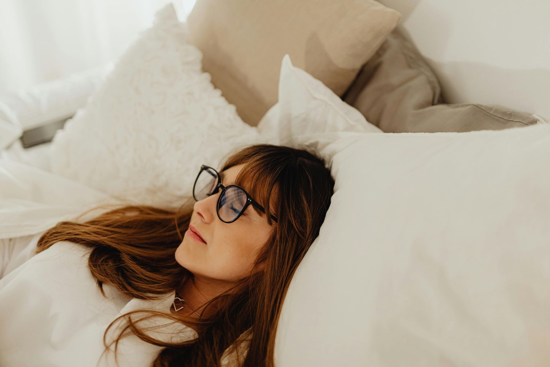 Woman laying down on a bed of white pillows