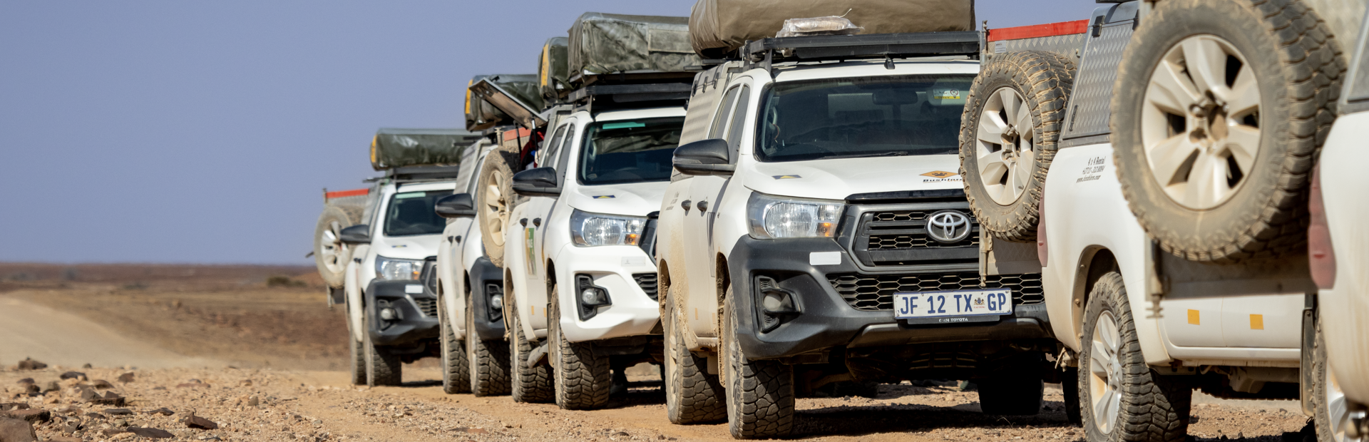a row of toyota hilux trucks are parked on a dirt road