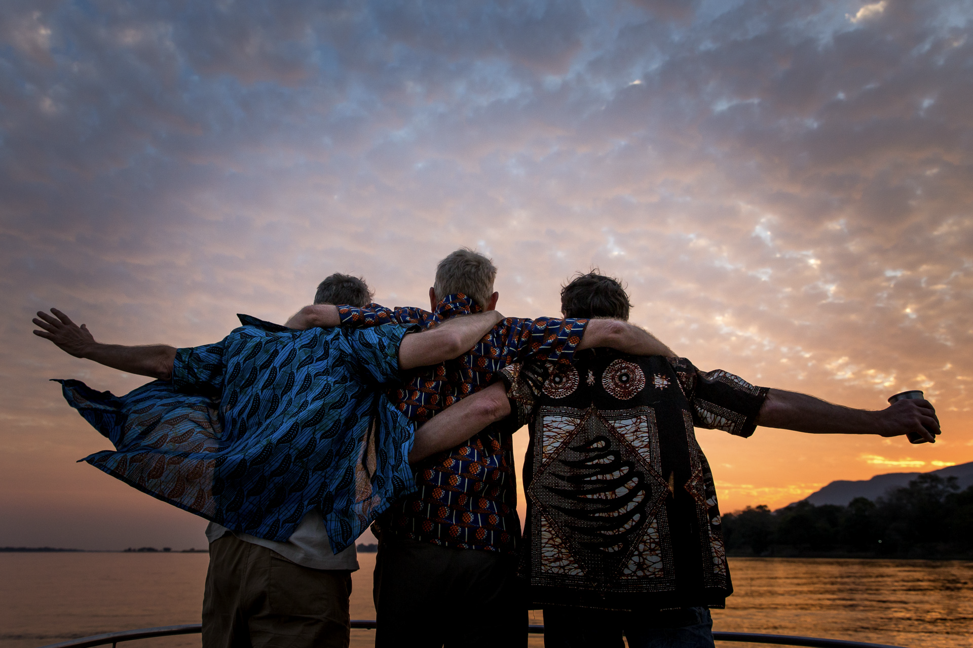 three men standing on a boat with their arms around each other