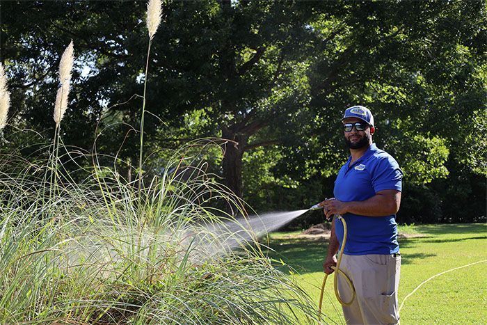 A man is spraying grass with a hose in a park.