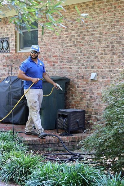 A man is holding a hose in front of a brick building.