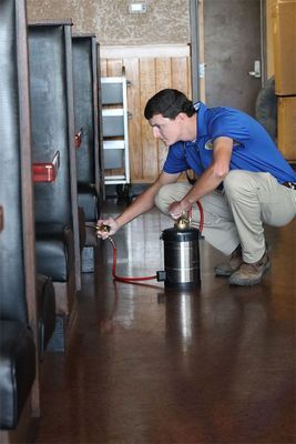 A man is kneeling down in a restaurant holding a spray bottle.