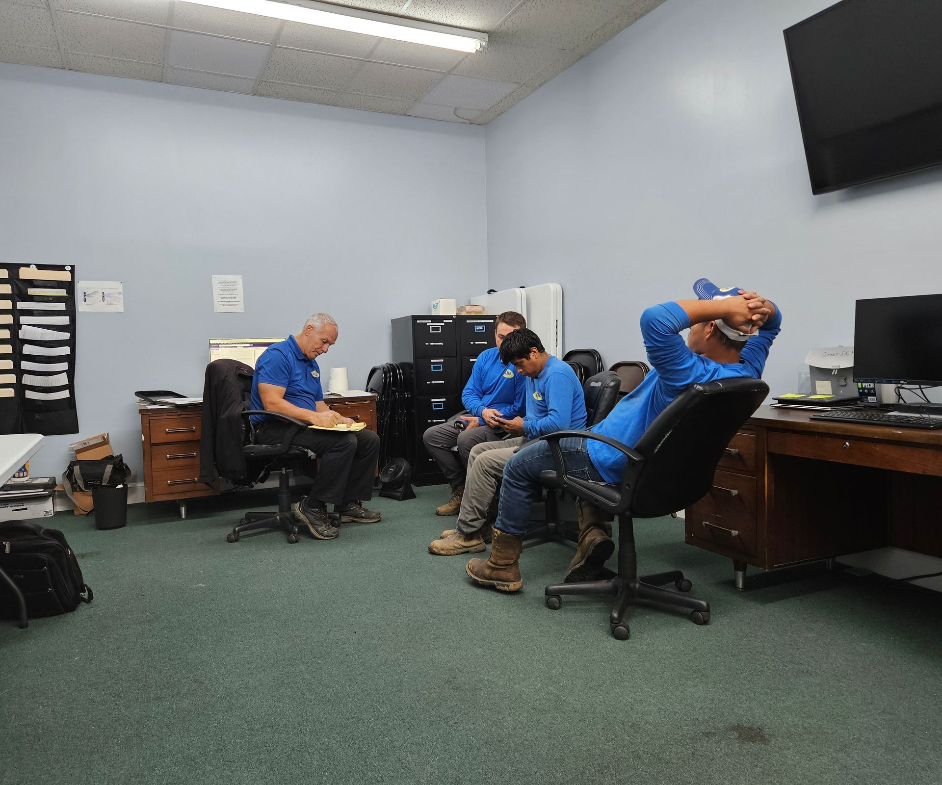 A group of men in blue shirts are sitting in an office
