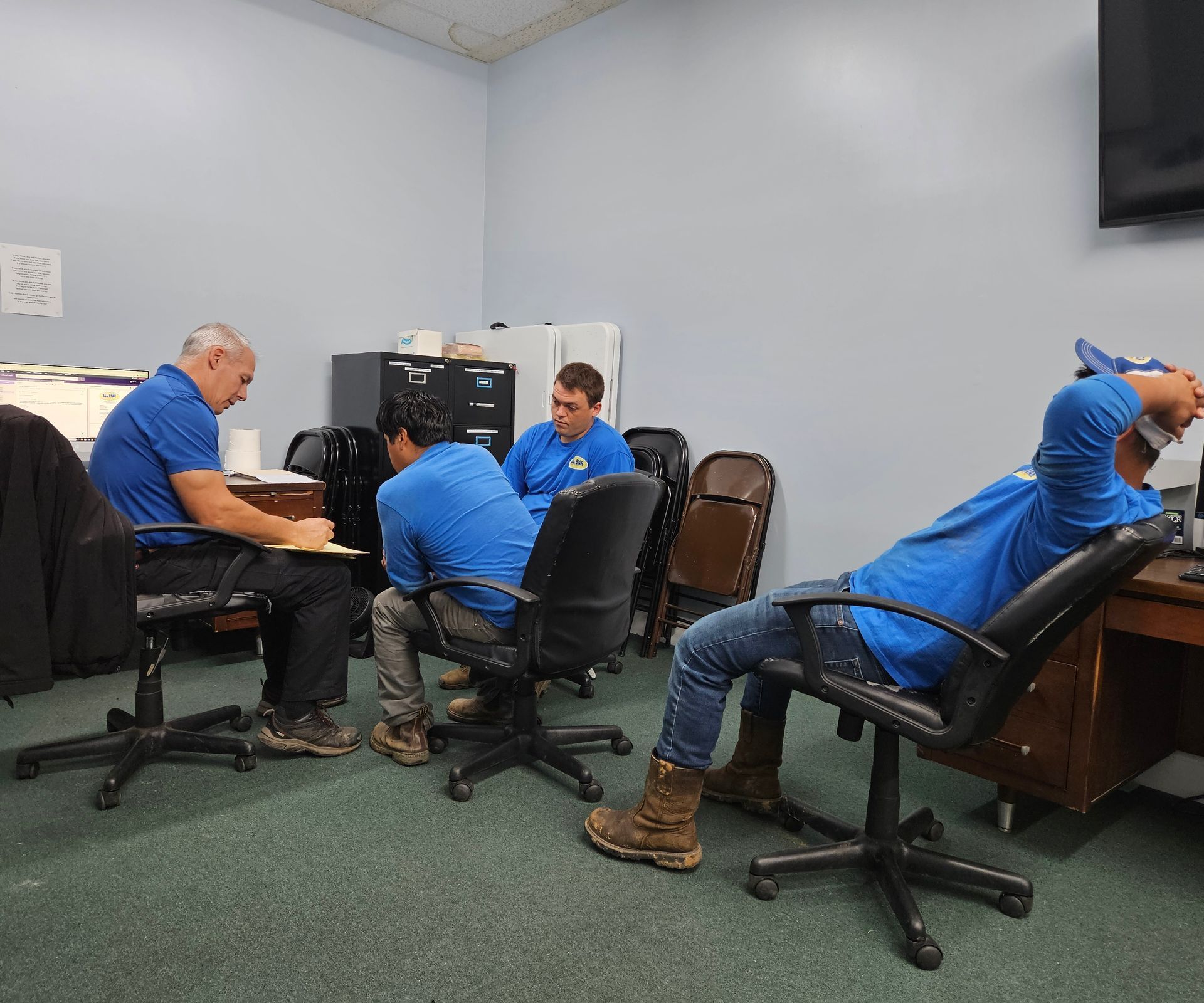 A group of men in blue shirts are sitting in chairs in an office