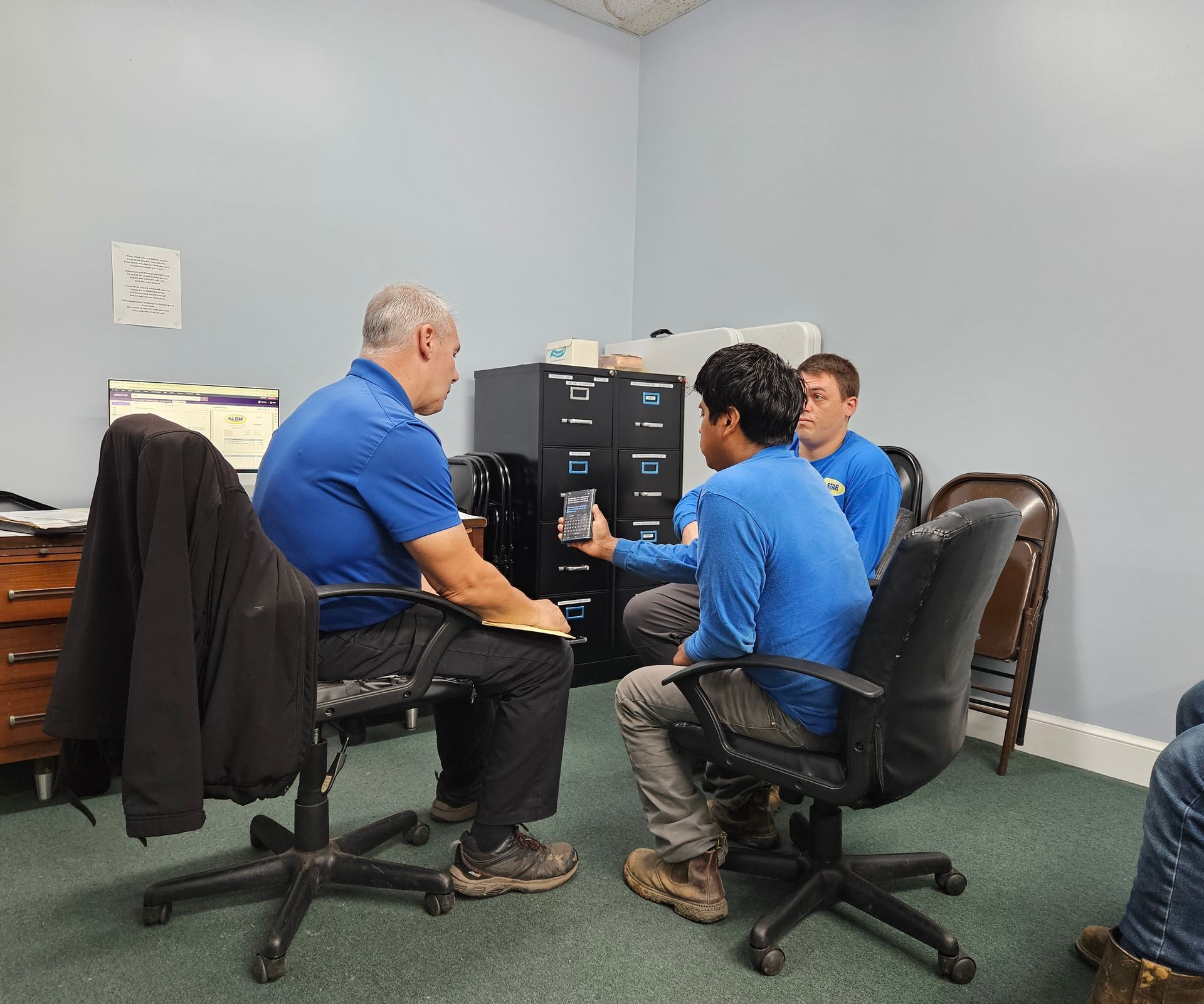 Three men in blue shirts are sitting in chairs in a room