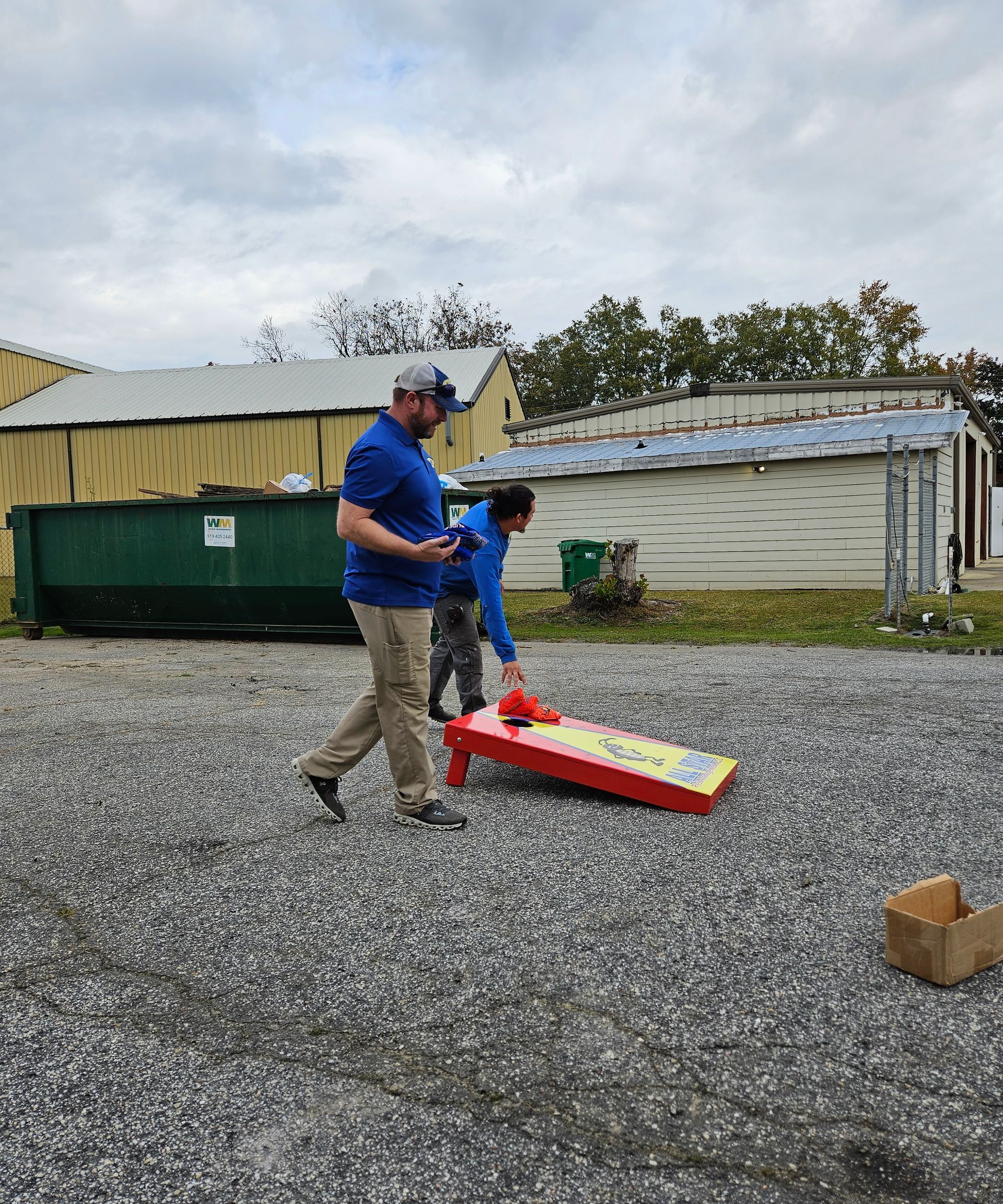 A man and a boy are playing cornhole in a parking lot.