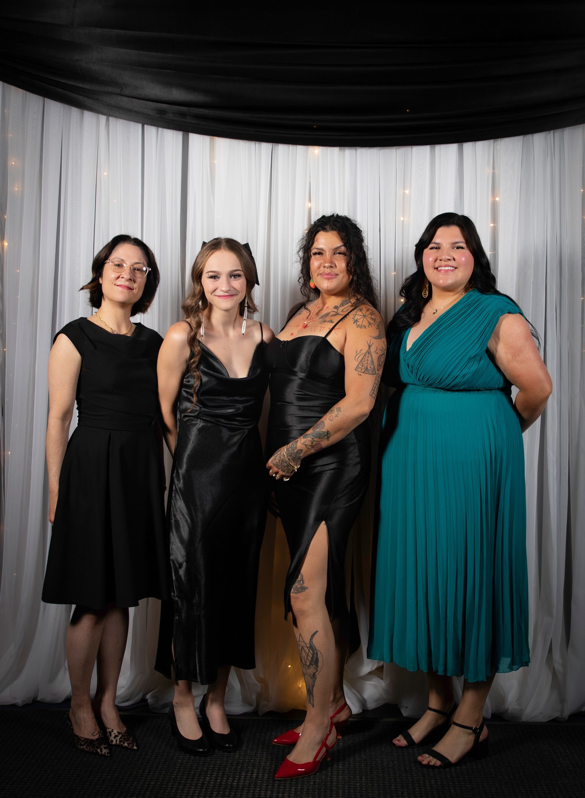 Four women in formal wear pose against a draped backdrop.