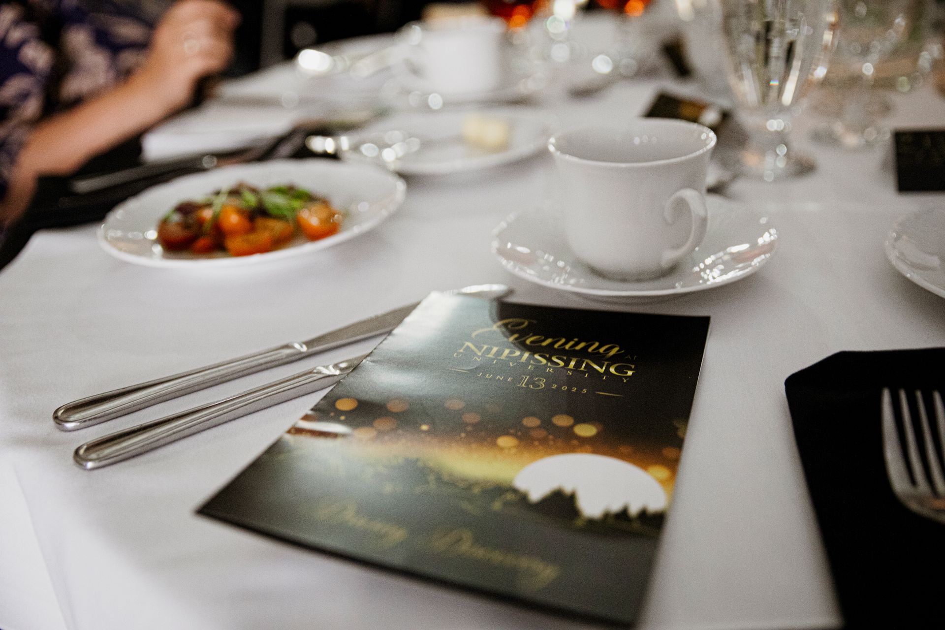 Elegant table setting with menu, food, silverware, and teacup at a formal event.