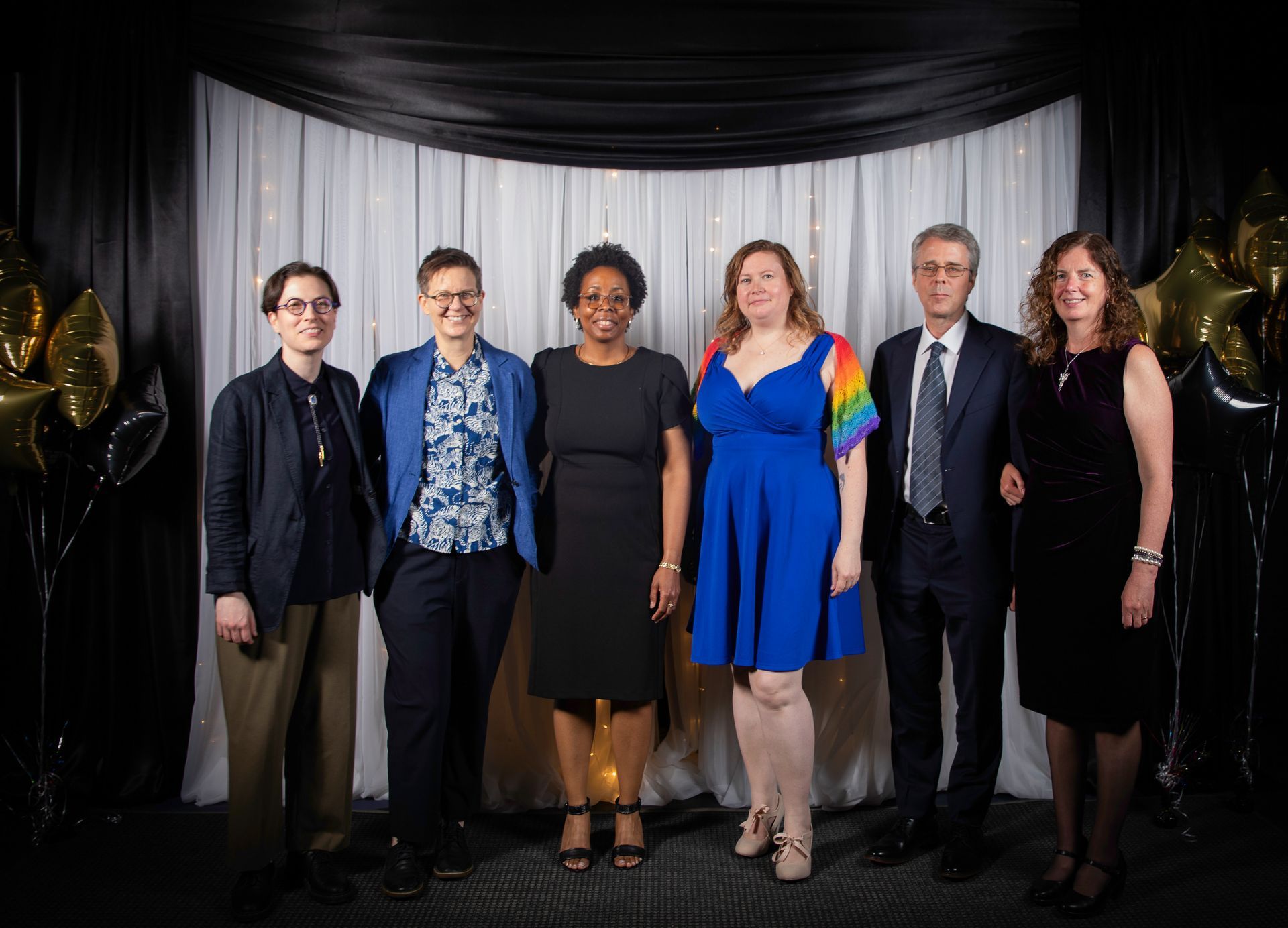 Group of six people posing for a photo in front of a black and white backdrop.