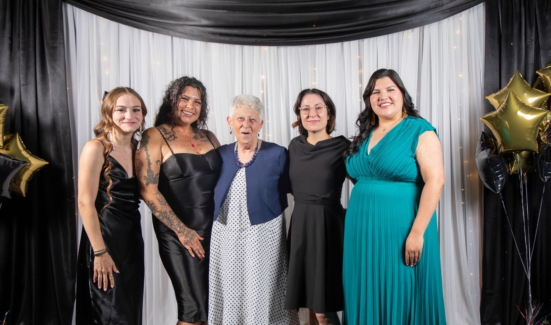 Five women pose for a photo in front of a black and white backdrop.