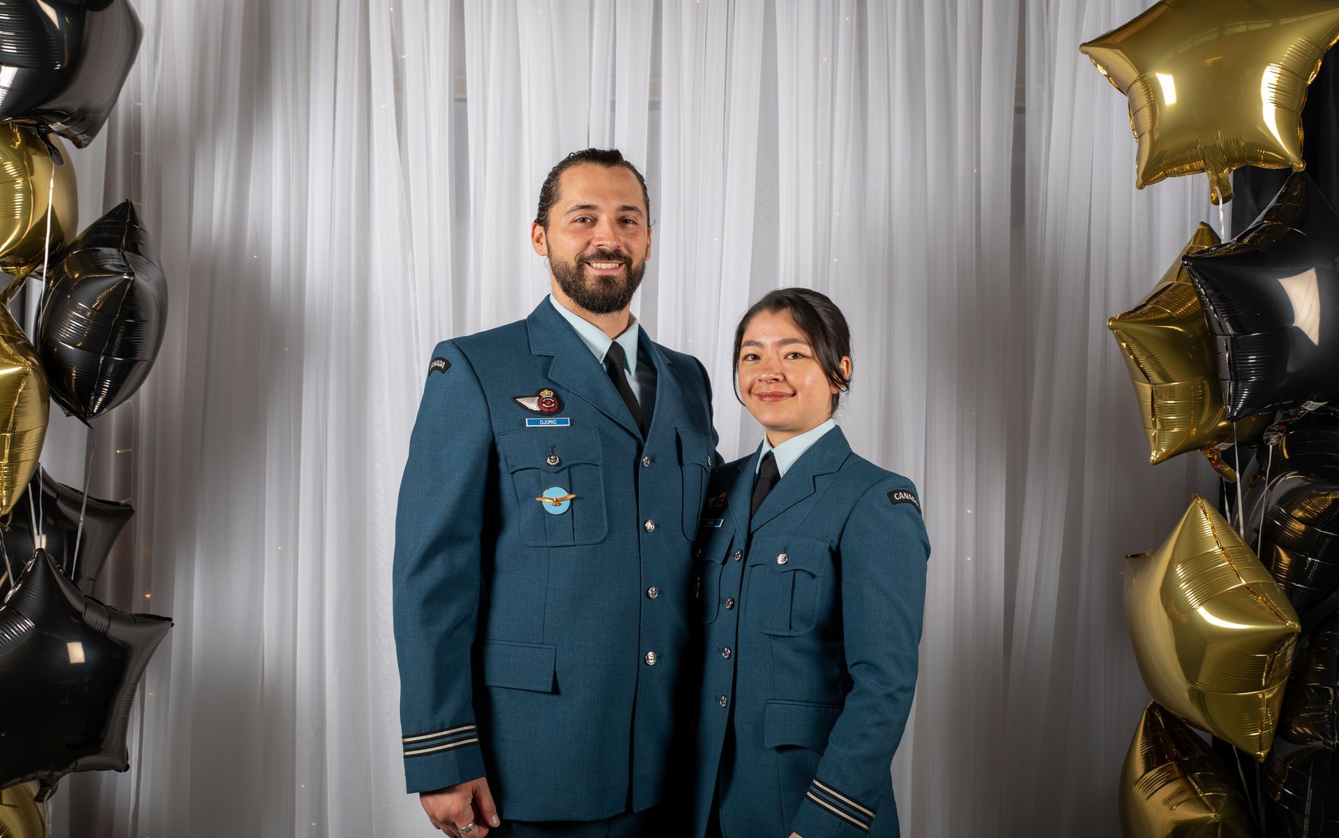 Two people in air force uniforms pose with balloons.