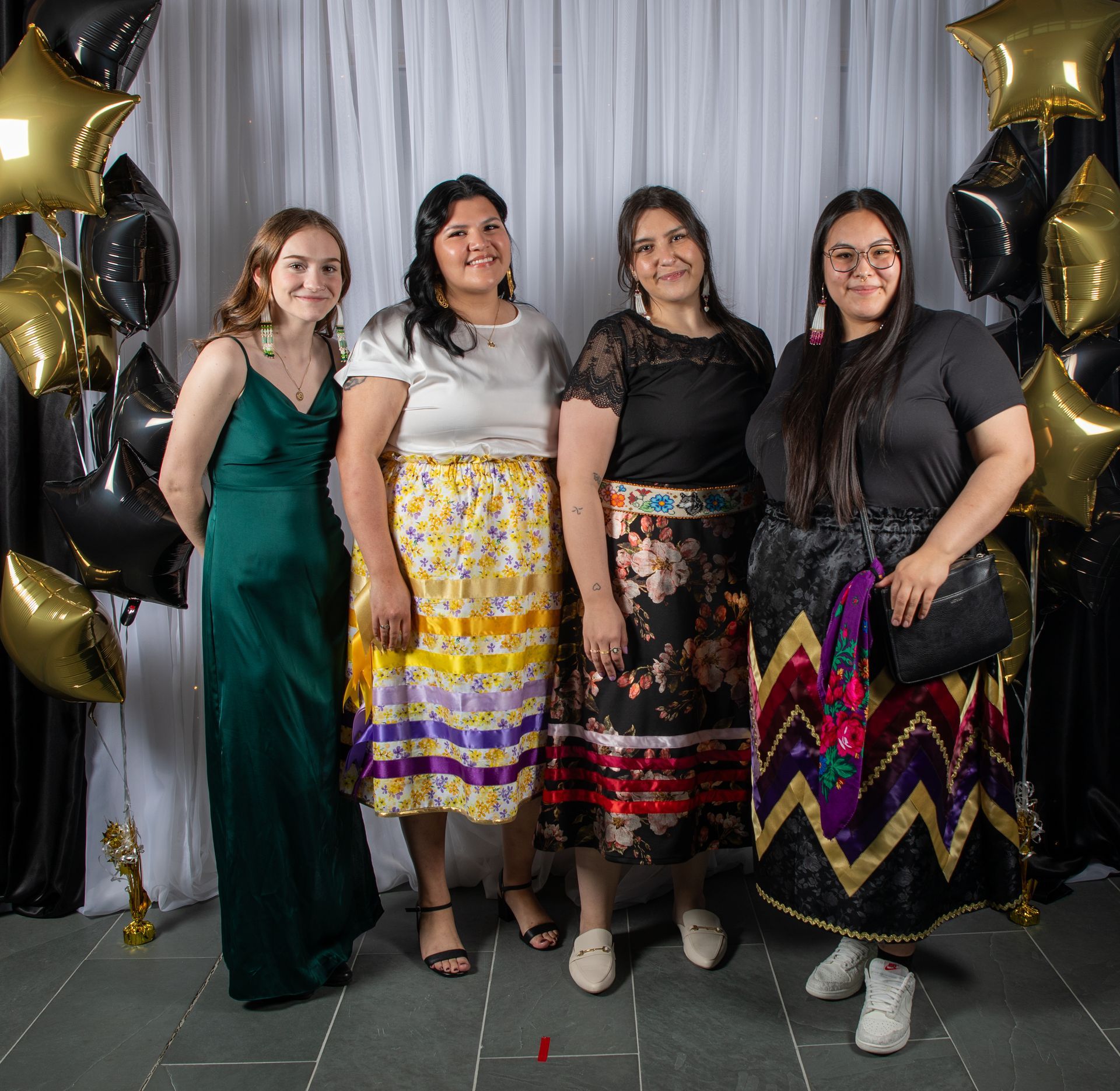 Four women smiling, posing for a photo in front of a white backdrop with balloons. 