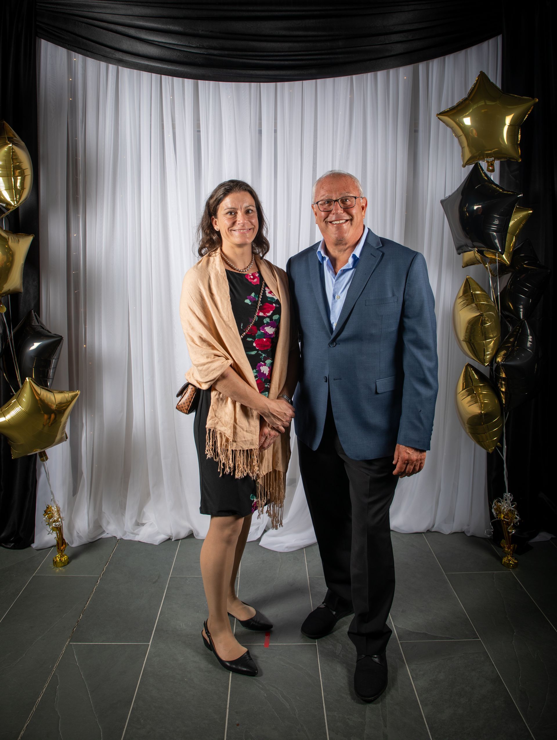 Couple posing in front of a black and white backdrop with gold and black star balloons.