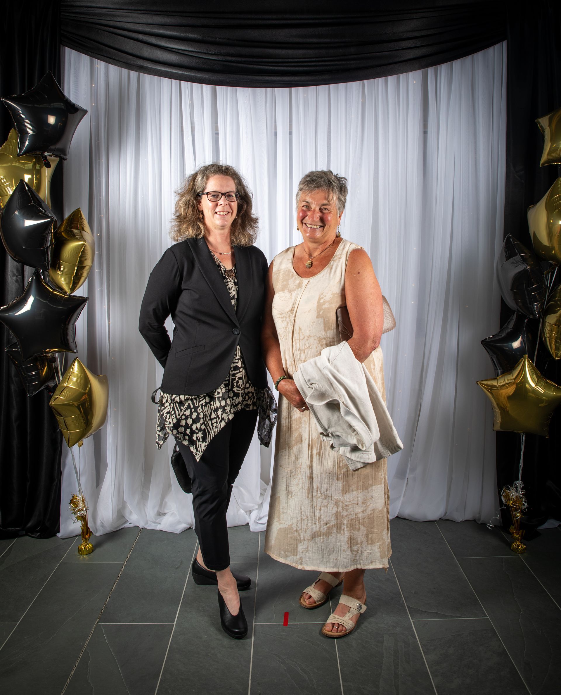 Two women pose for a photo at a formal event with black and gold star balloons.