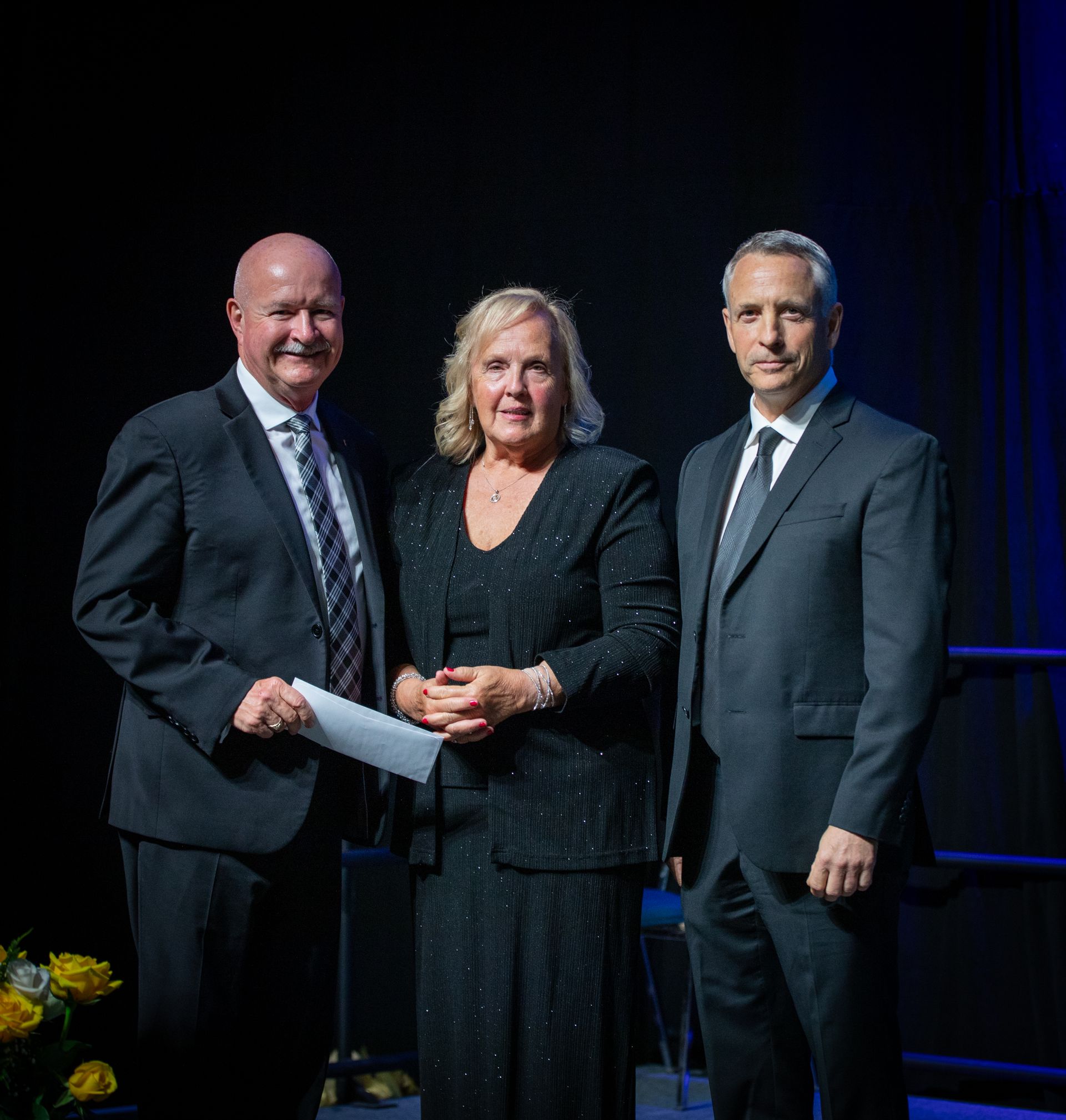 Three people in formal attire on stage, receiving an award.