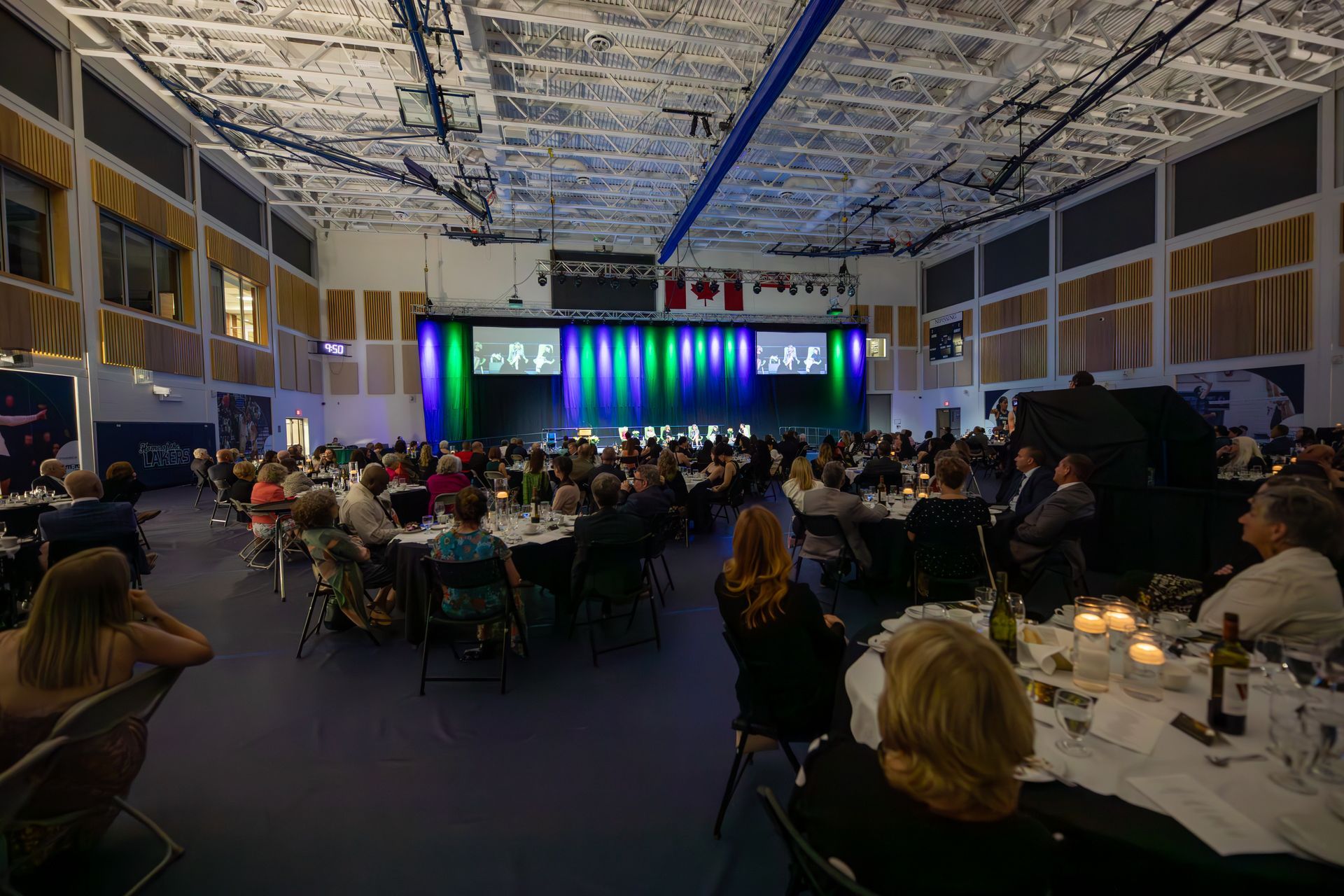 Large event hall with seated guests at tables, stage with a colorful backdrop.