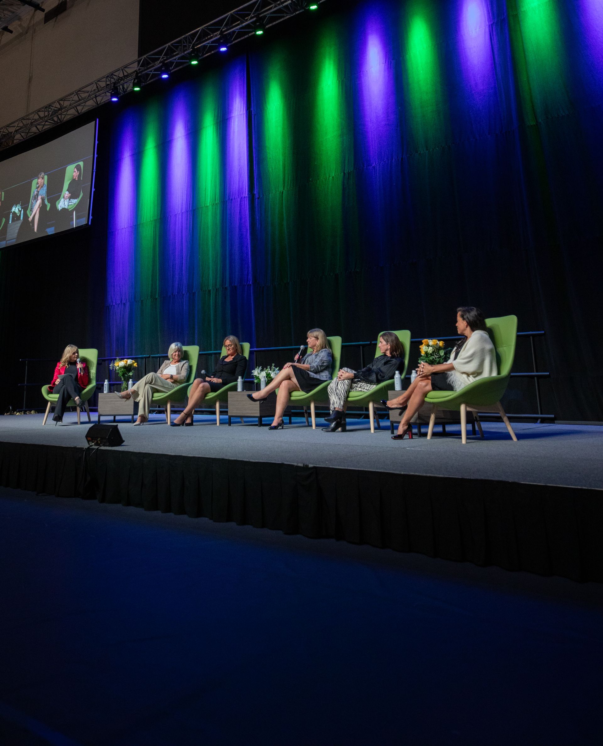 Panel of women seated on stage with green and blue lighting.