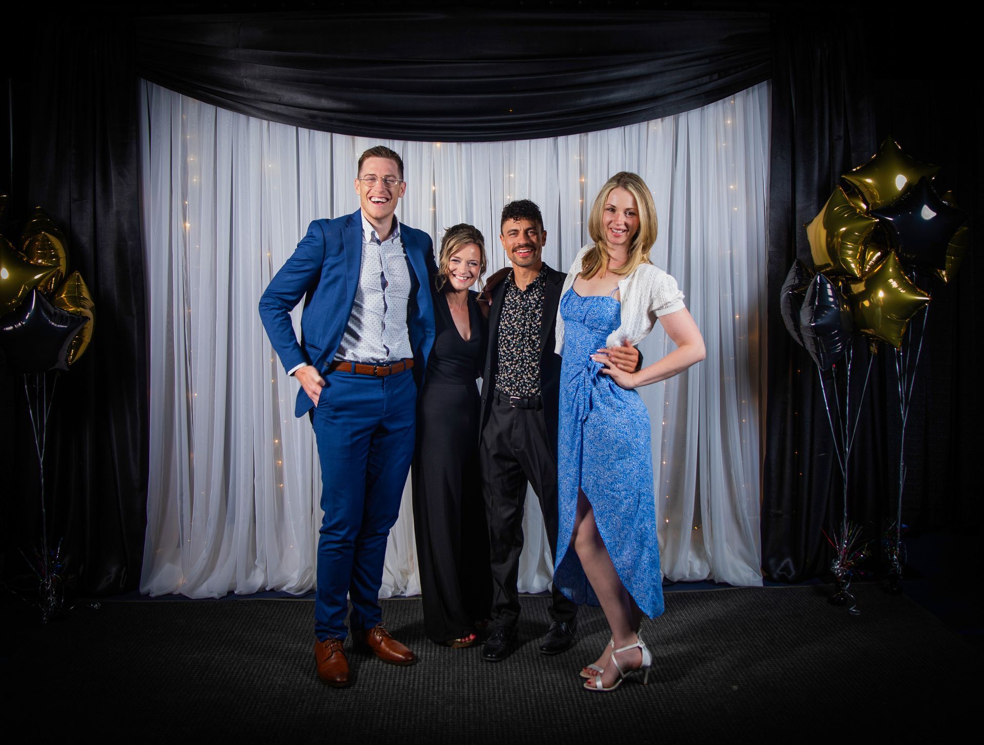 Four people pose for a photo in front of a black and white backdrop with balloons.