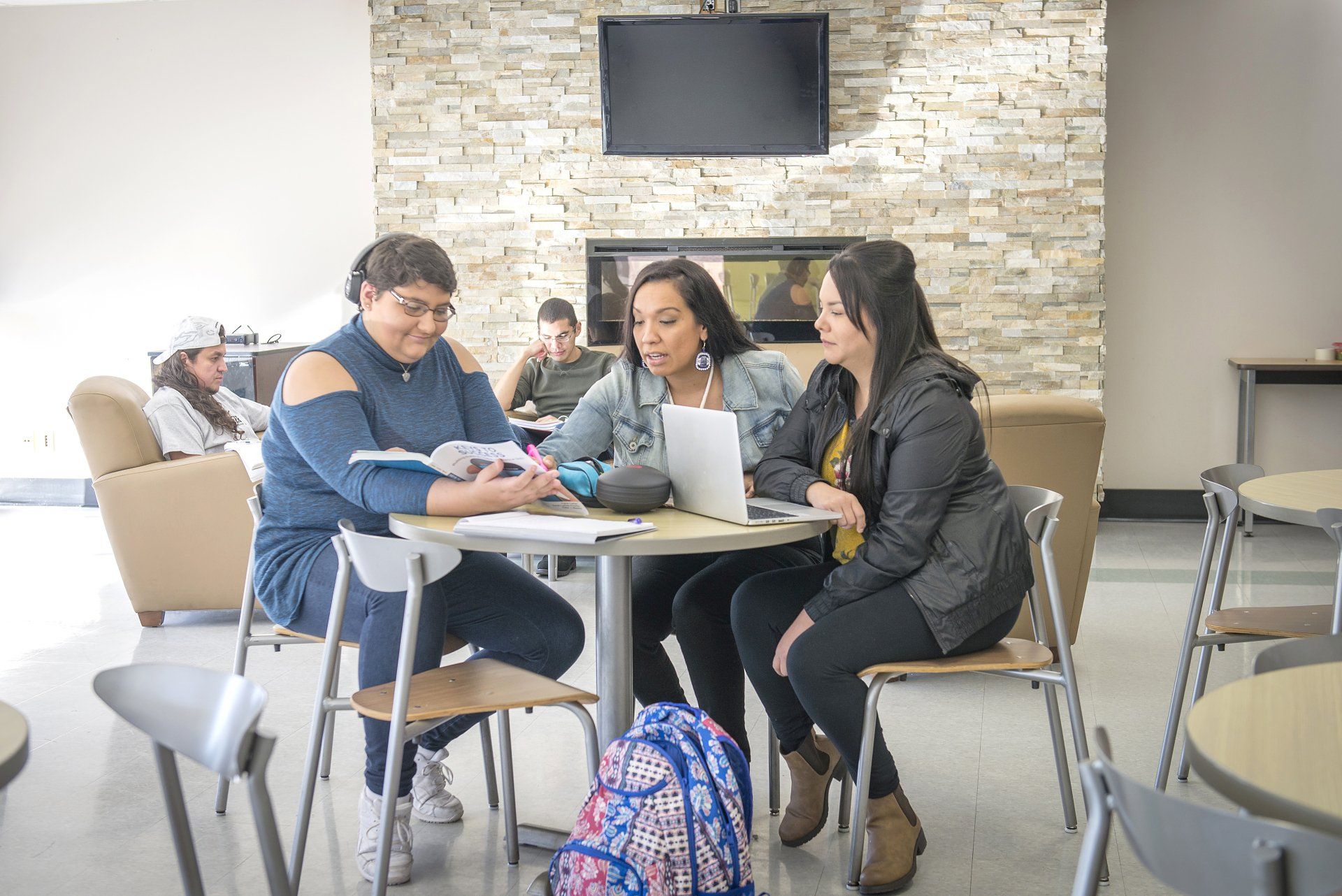 Three women study around a table with a laptop. They are focused and sharing ideas in a well-lit space.