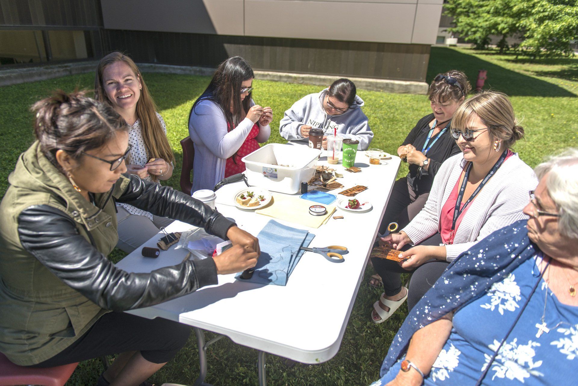 Group of women crafting at an outdoor table on a sunny day.
