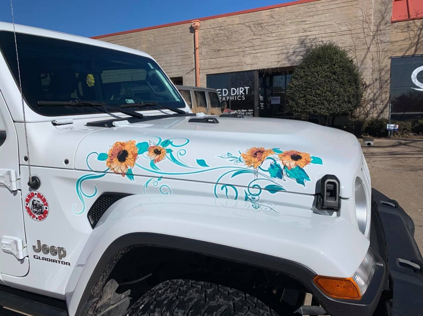 White Jeep with sunflower decals parked outside a building.