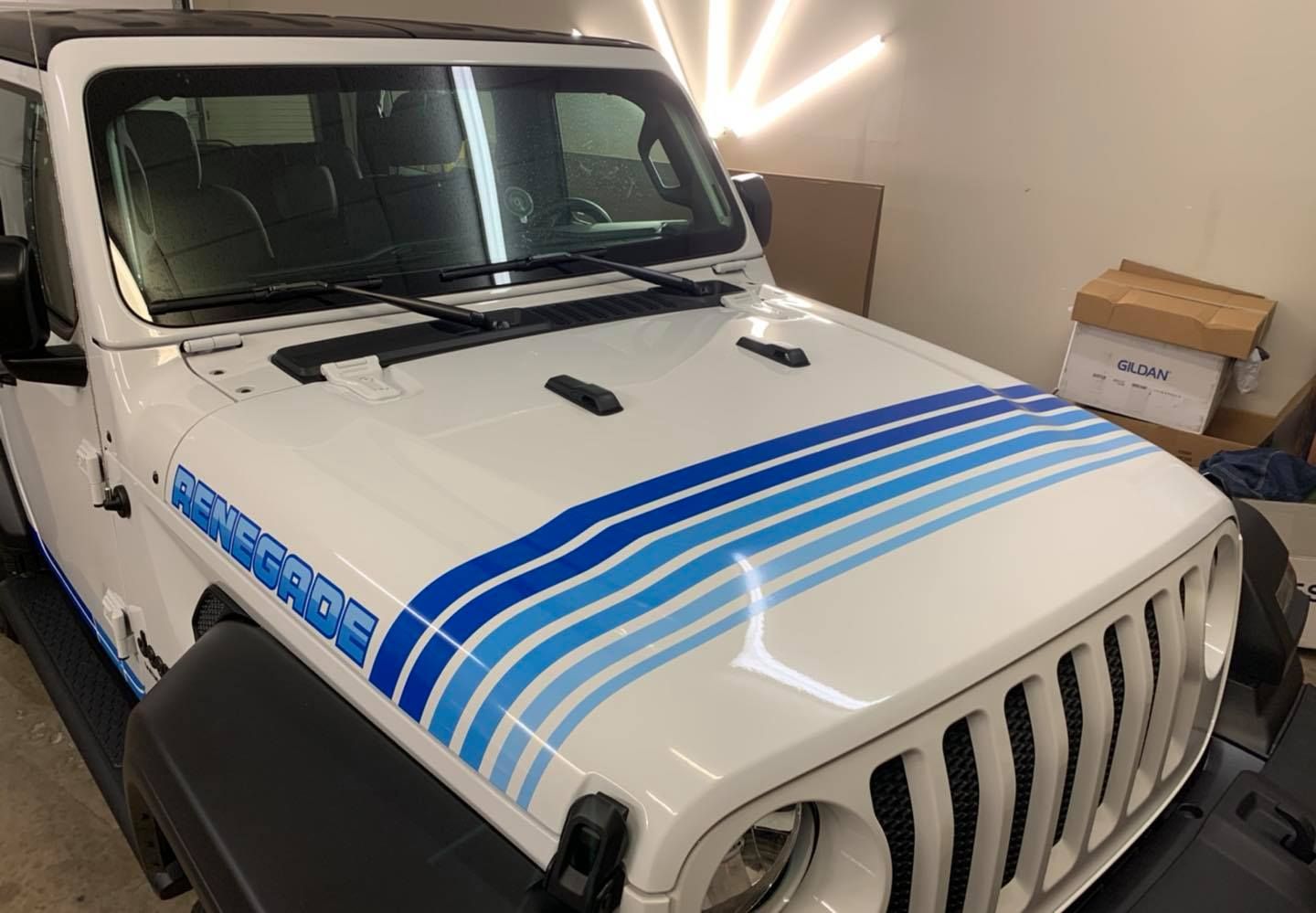 White Jeep with blue stripe decals on hood; indoors, in a garage-like setting.