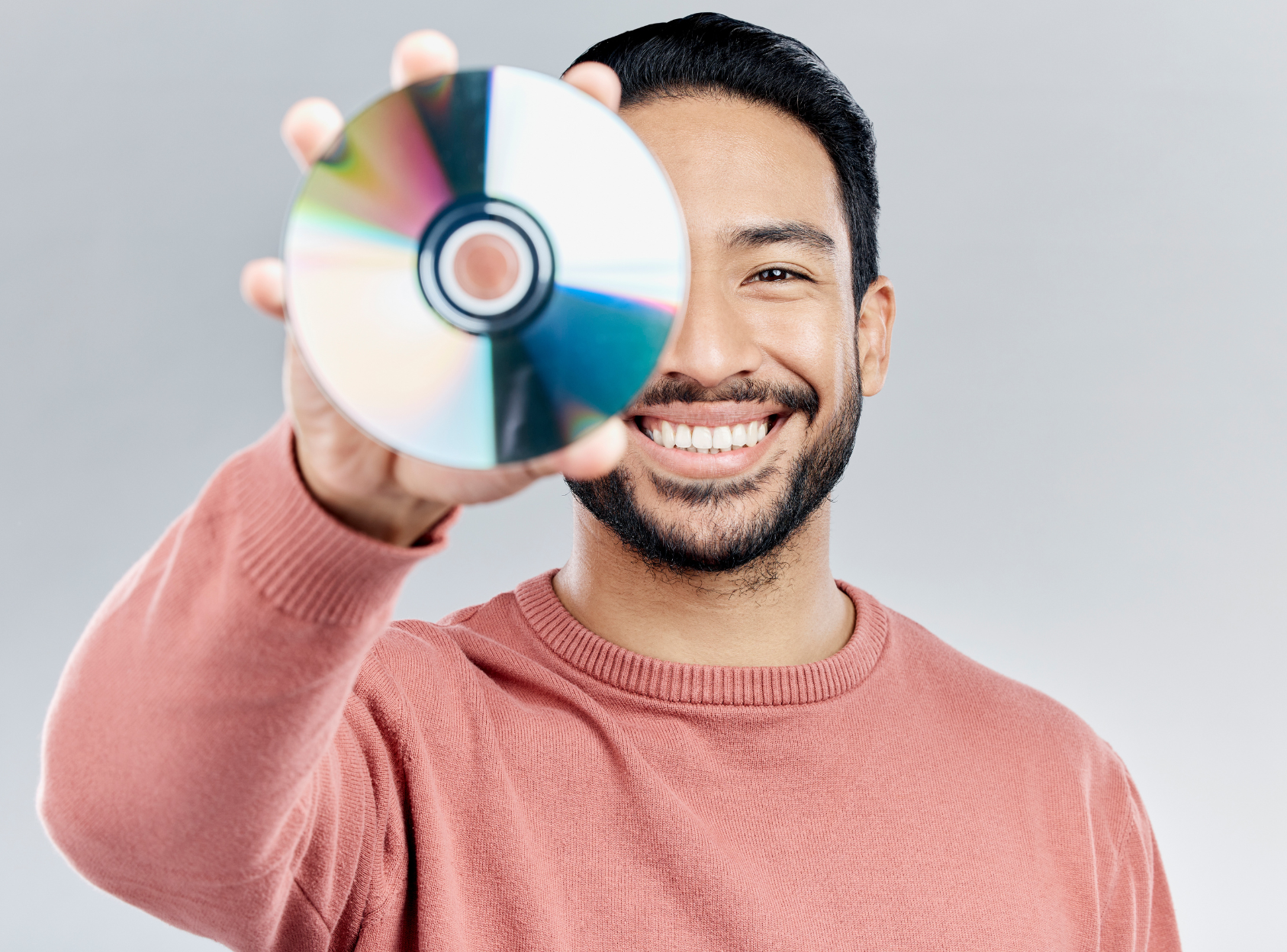 A man in a pink sweater is holding a cd in front of his face.