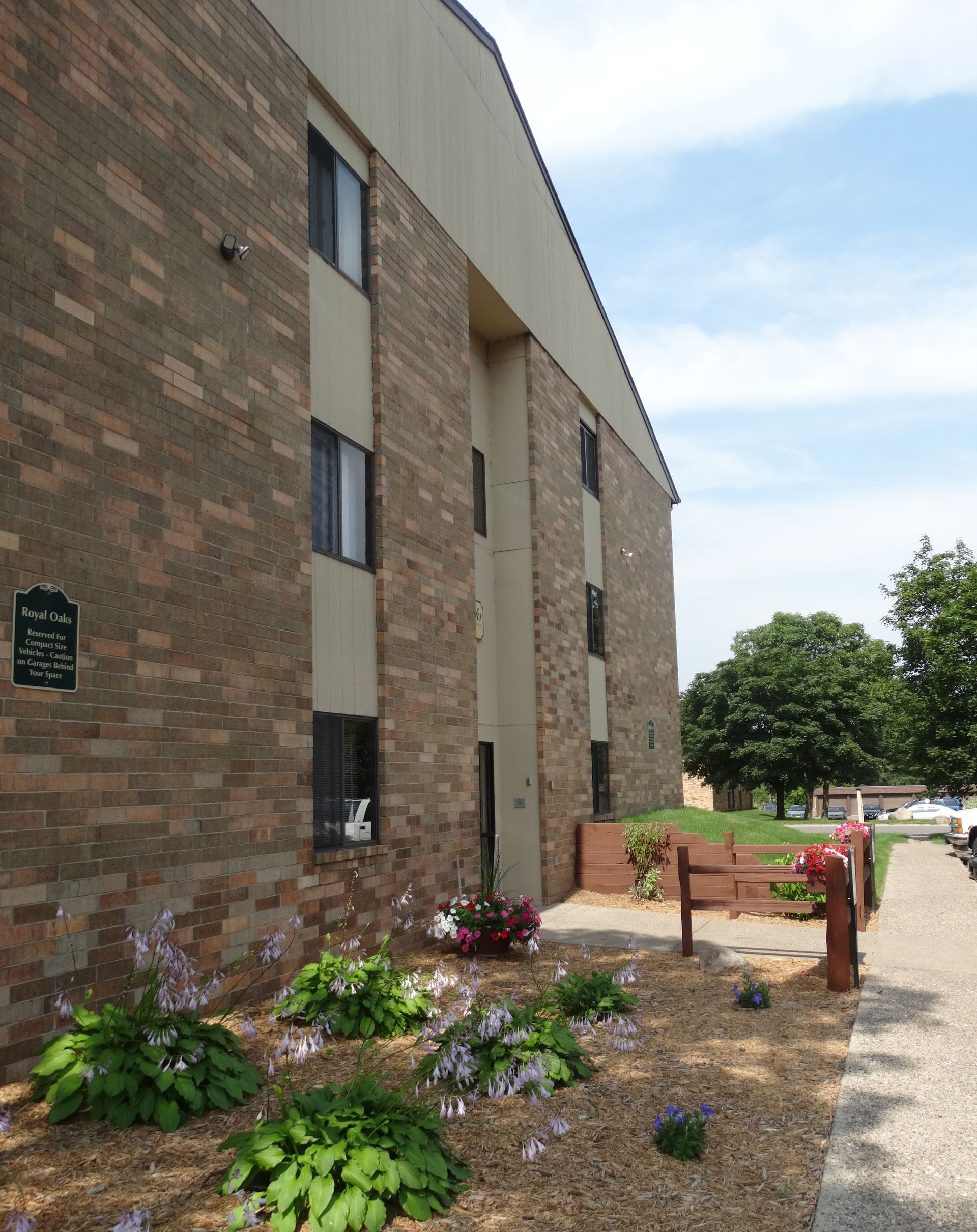Brick apartment building with landscaped beds, blue flowers, and a gravel path.