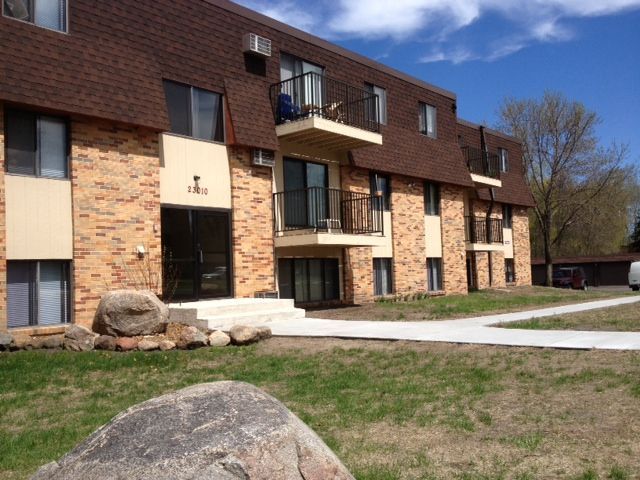Apartment building with brown roof and tan brick exterior, blue sky.