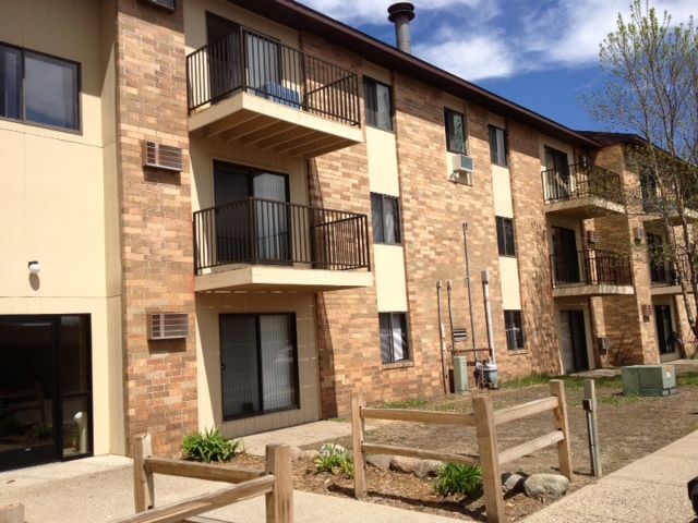 Apartment building with brick facade, balconies, and a wooden fence in front.