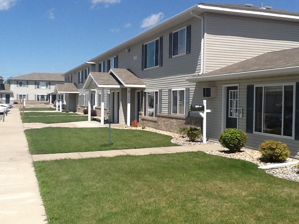 Row of multi-unit residential buildings with green lawns and sidewalk in front.