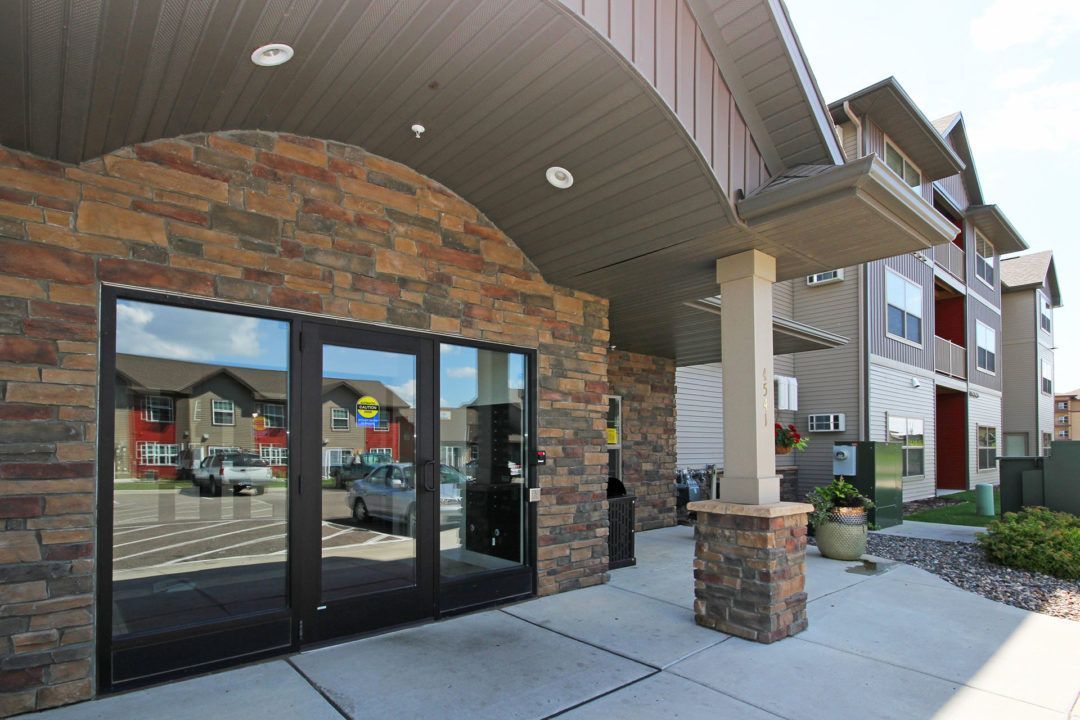 Entrance to a modern apartment building with stone facade, glass doors, and covered walkway.