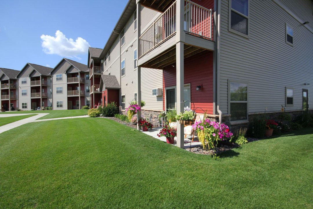 Apartment complex exterior with balconies, red accents, and green lawn.