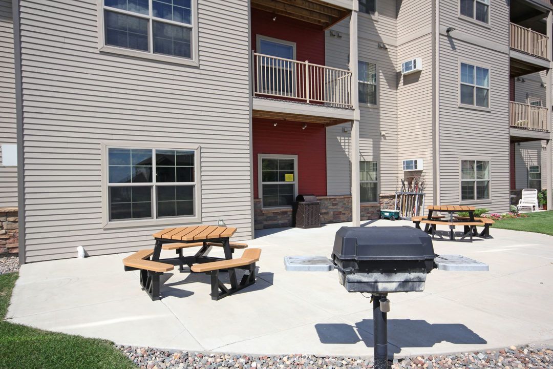 Outdoor patio with picnic tables and a grill next to an apartment building.